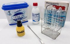Metal rack with glass test tubes, spatula, plastic bottles, plastic and cardboard boxes of different sizes containing reagents and detergents.